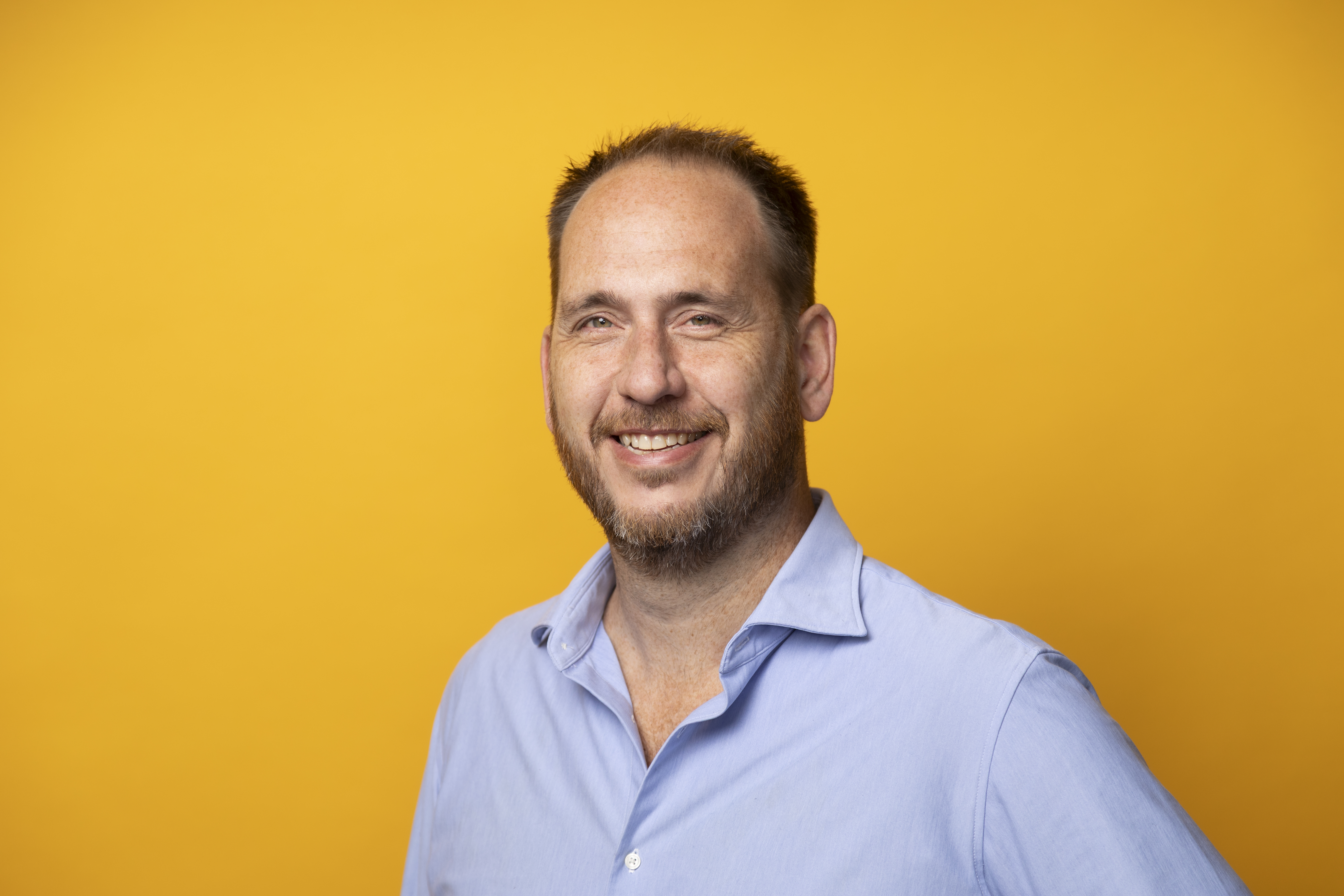 Een man in een blauwe blouse tegen een gele achtergrond.
