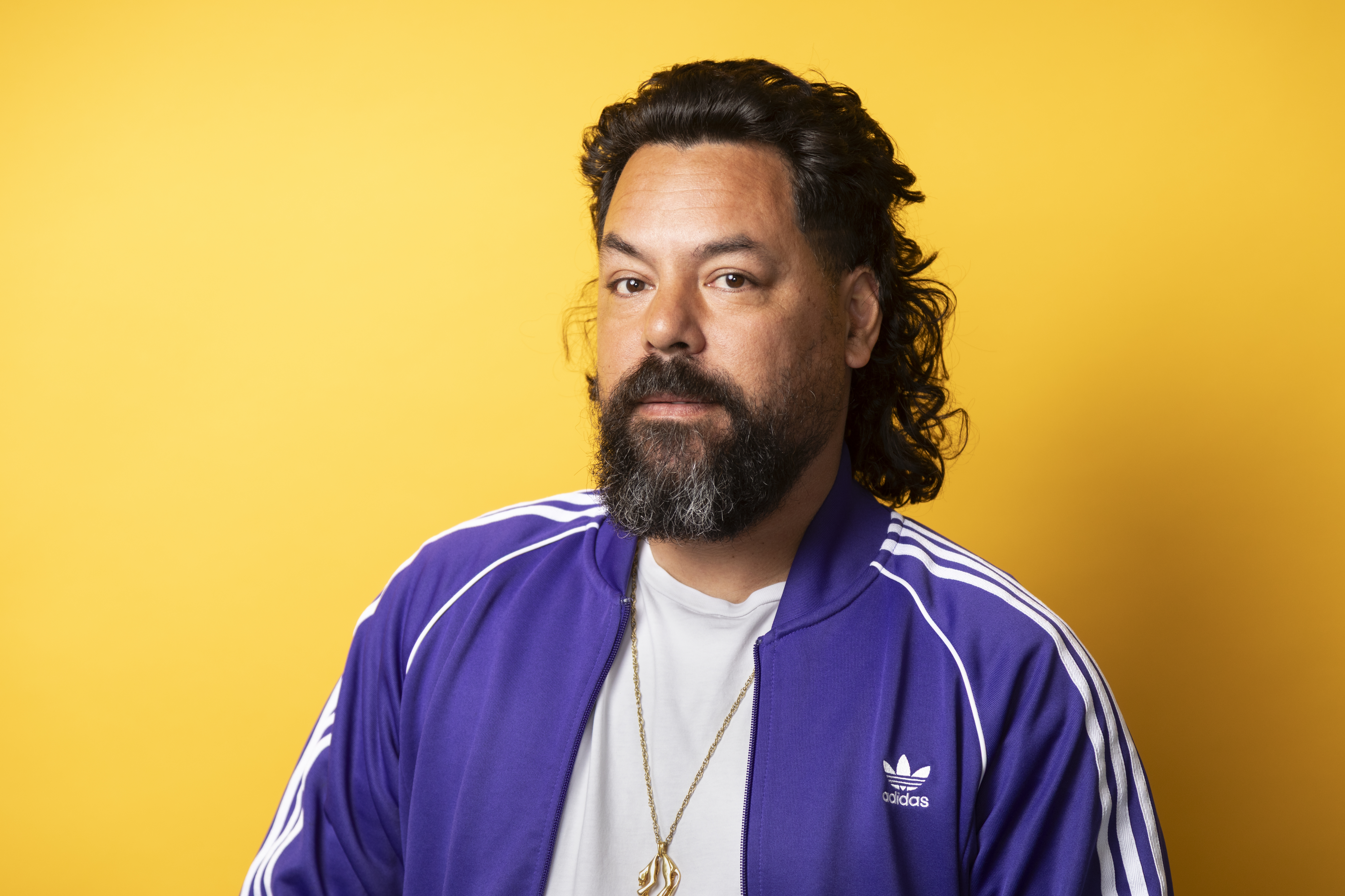 Een man in een trainingsjack tegen een gele achtergrond.