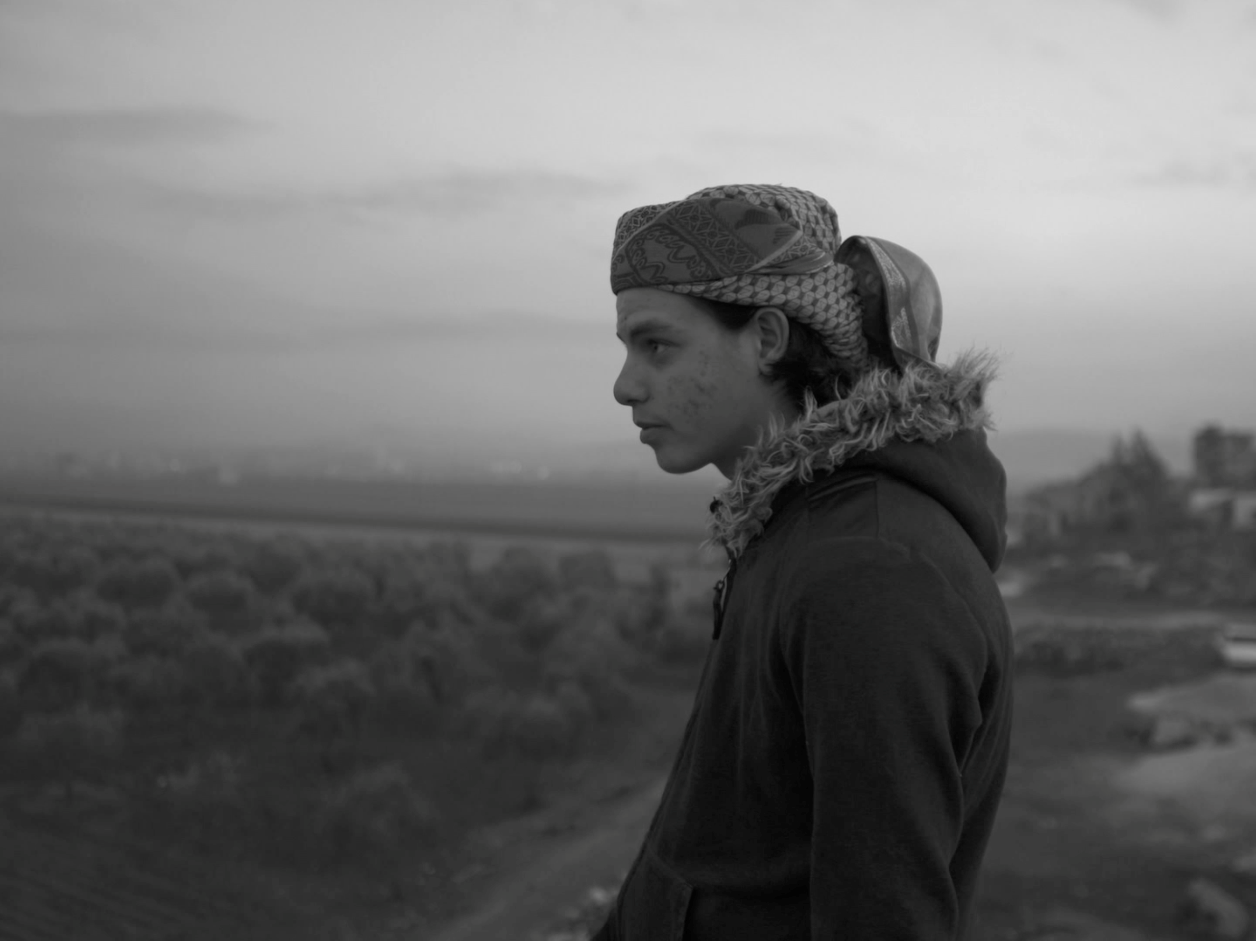 Zwart-witfoto van een jongen die in de verte kijkt.