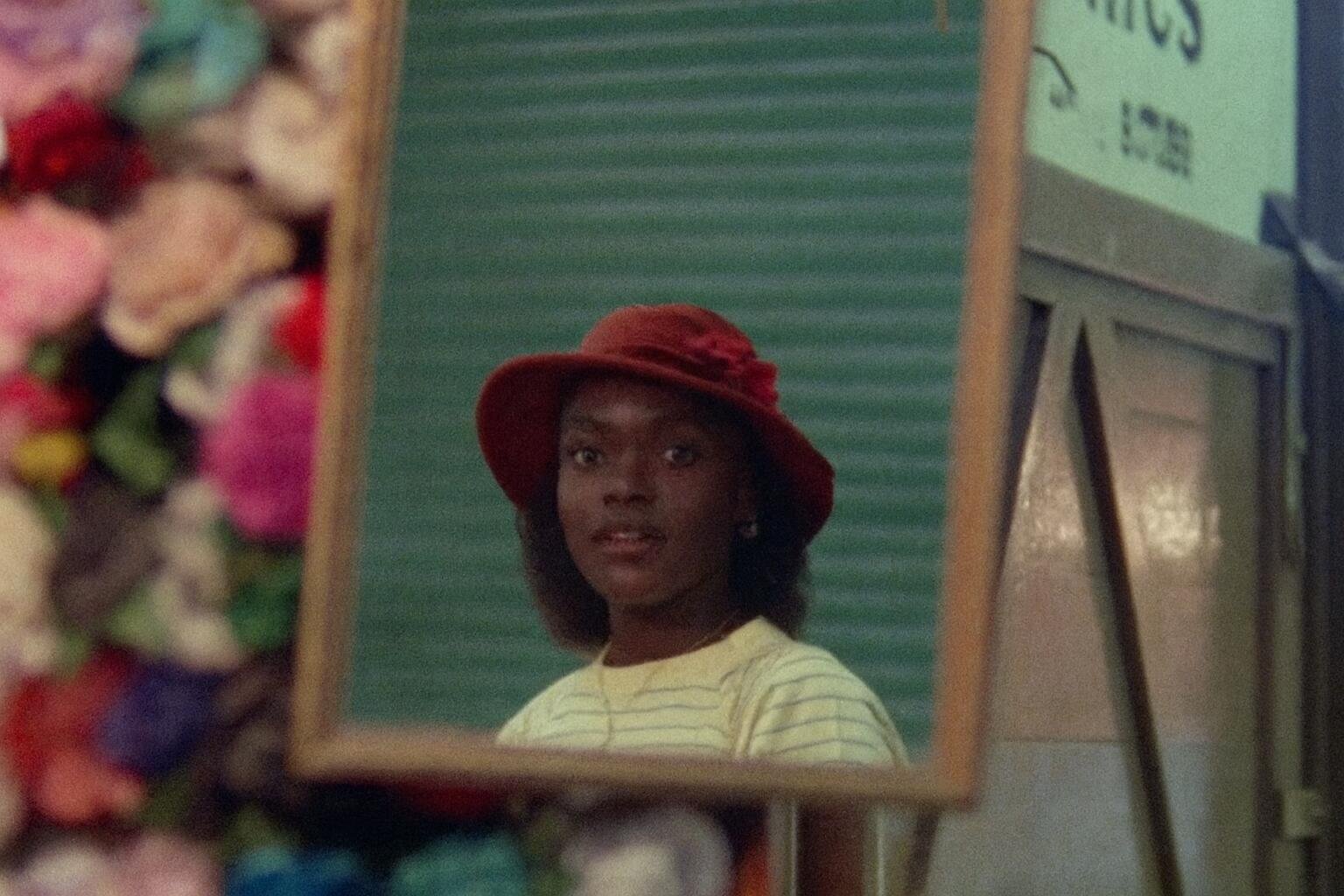 A girl wearing a hat looking into a mirror.