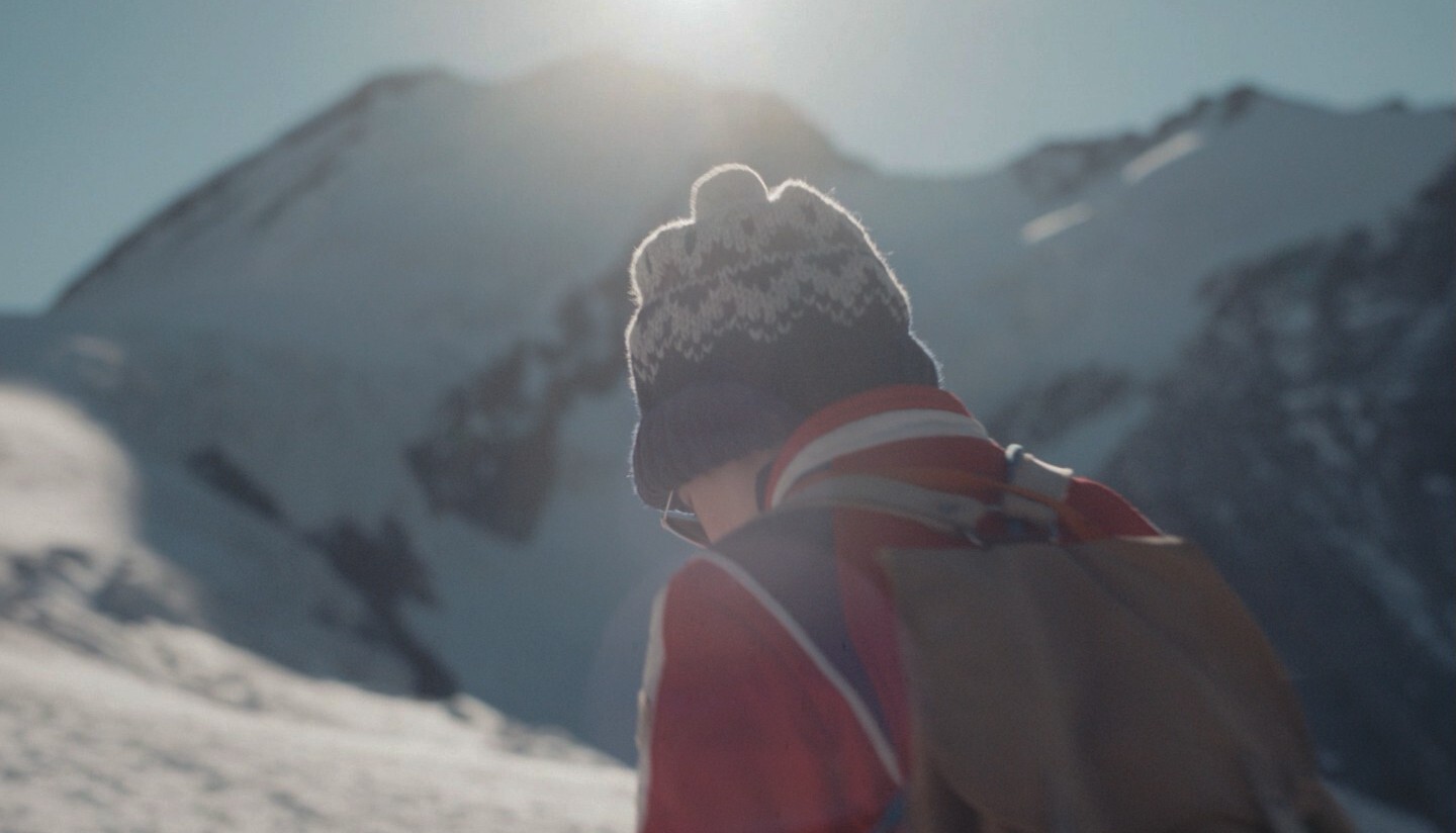 Een persoon met een muts op in een besneeuwde bergomgeving.