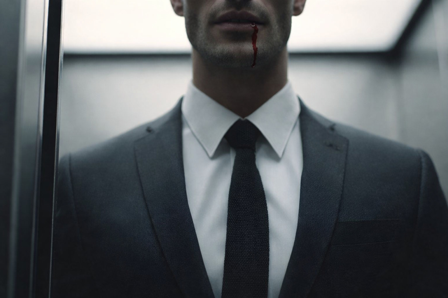 Een man in een pak staat in een lift, er loopt bloed uit zijn mondhoek.